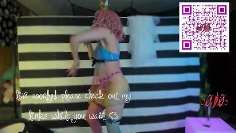 A video of a curvy woman with pink hair, wearing a blue bra and pink garter belt, in a striped room with a QR code overlay.
