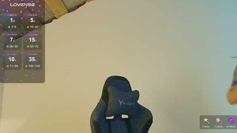 Media: A video captures a dark blue gaming chair with a plush, cushioned backrest, positioned against a plain beige wall. The image features a digital overlay displaying a \"Lovense\" menu, indicating it's a sex toy.