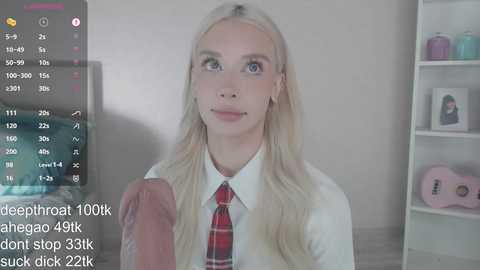 Video of a blonde, fair-skinned woman in a school uniform, holding a large erect penis. Background shows a white shelf with knick-knacks. Text overlay: \"deneb_gar 100k ahlega 49k don't stop 33k suck dick 22k.\