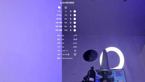 A video of a modern, minimalist room with purple lighting, featuring a white circular light fixture and a large, white, round moon-shaped object. The room is clean and sleek, with a digital display on the left showing temperature and humidity levels.