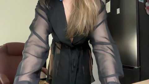 Video of a woman in a sheer black blouse, leaning over a desk in an office setting.