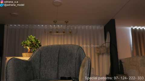 Video of a dimly-lit living room featuring a plush, textured blue sofa, a potted plant, and a chandelier with multiple golden lights. The background shows sheer white curtains. Text reads \"Special patterns 97-144-2223\" and \"Alexa, read the story to me!\