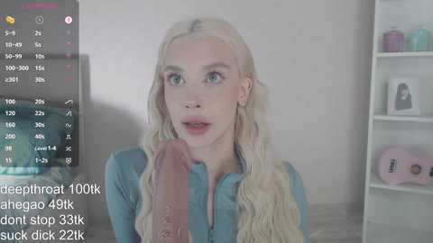 Media: A video of a blonde woman with fair skin and blue eyes, wearing a blue top, looking surprised. A penis is visible in the foreground.