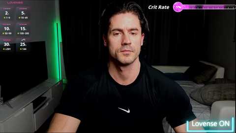 A video of a man with long dark hair, wearing a black shirt, sitting in a dimly lit living room. A TV screen displays \"Love Island ON.\