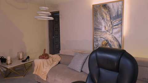 Video of a modern living room featuring a beige sectional sofa with a cream throw, gold coffee table, large abstract painting, black leather chair, and minimalist decor.