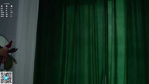 A video of a person standing behind a green curtain with a red bow tie and a white shirt, holding a red-and-white polka-dotted balloon, viewed from the side.
