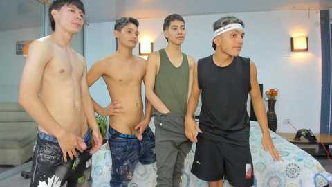 Video of four shirtless, lean Asian men in casual attire, standing in a modern bedroom with a bed, lamps, and minimalist decor.