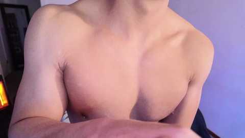 Video of a light-skinned, shirtless man with a toned physique, focused on his upper torso and shoulders. Background includes a purple wall and indistinct furniture.