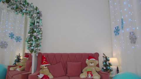 Video of a festive living room with a pink sofa, Christmas decorations, and two large teddy bears dressed as Santa Claus.