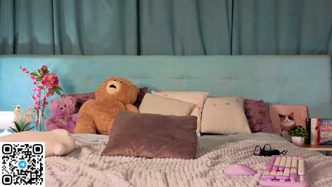 Video of a cozy bedroom with a light blue headboard, a teddy bear, pillows, books, and a QR code in the lower left corner.