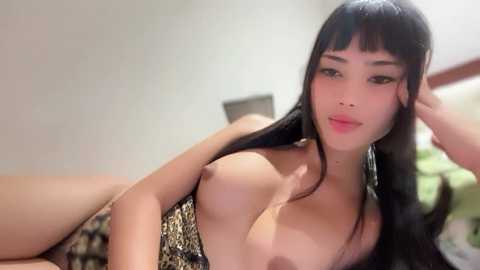 Media: Video of an Asian woman with long black hair, wearing a leopard-print bikini top, exposing her medium-sized breasts. She is reclining on a bed with a blurred background.