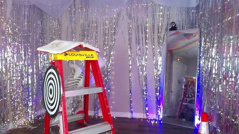 A video of a room decorated with silver tinsel, a red and white \"Lowe's\" ladder, and a reflective disco ball, creating a festive, retro atmosphere.