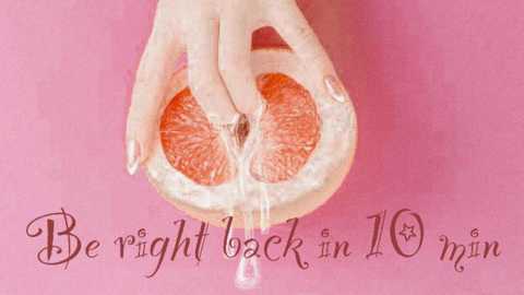 A video of a hand holding a half-peeled orange, with a drop of juice, set against a pink background. Text reads \"Be right back in 10 mins.\
