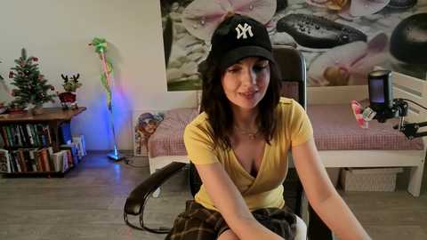 Media: A video of a woman with long black hair, wearing a New York Yankees hat and yellow top, sitting in a chair in a cozy, book-filled room with a Christmas tree and a large fish poster.