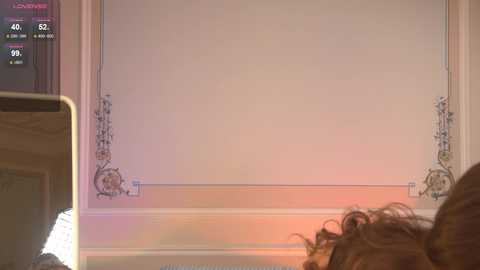 Video of a person with shoulder-length curly brown hair, partially visible, holding a smartphone, looking at a white wall with ornate, floral-patterned trim, with a digital clock displaying 4:50 AM, and an ambient warm light.