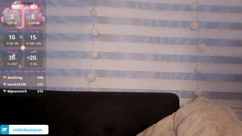 A video of a bedroom with a black headboard and white and blue striped wallpaper. A digital clock with a yellow background displays the time, temperature, and weather conditions.