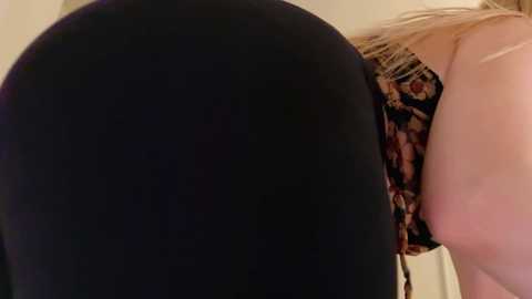 Video of a close-up of a woman's buttocks in tight black leggings, with a glimpse of her blonde hair and floral-patterned top in the background.