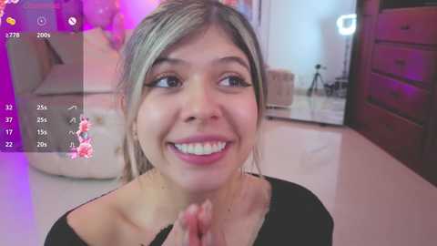 Video of a happy, light-skinned woman with blonde hair, wearing a black top, in a modern, brightly lit room.