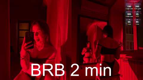 A video captures a woman with long brown hair, wearing black lingerie, taking a mirror selfie in a dimly lit room bathed in red light. Text reads \"BBR 2 min.\