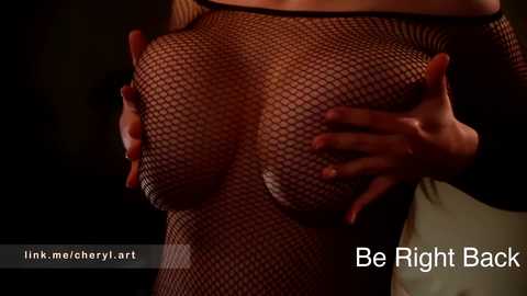 Video of a light-skinned woman wearing a black fishnet top, revealing her large, round breasts. Her hands are cupping her breasts. The background is dark, with text overlaying \"Be Right Back\" and \"link.me/cherry_art.\
