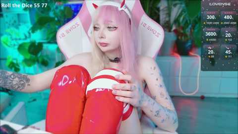 Video of a pale-skinned woman with pink hair in a white and pink \"ASUS\" headset, wearing red latex thigh-high boots and a red and white top, sitting on a gaming chair.