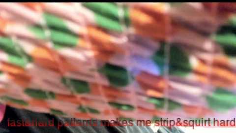 A blurred video of a quilted fabric with bright, geometric patterns in green, orange, and white, overlaid with the text \"lasagna makes me strip & squirt haro.\