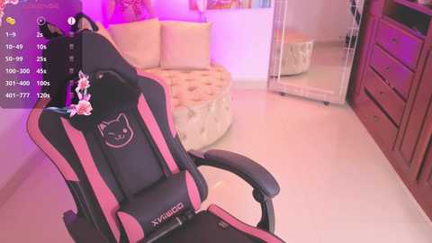 A video of a cozy gaming room with a pink and black gaming chair, a plush circular couch, and a wooden dresser.