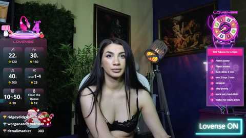 Video of a young woman with long black hair, wearing a black bra, sitting in front of a green screen with a virtual background.