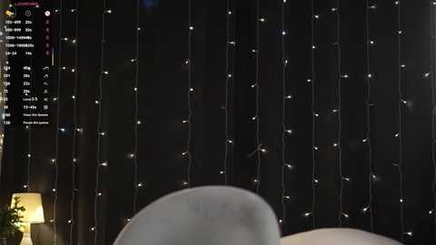 Video of a dark, starlit sky with string lights, blurred background, and a hint of a white, textured surface in the foreground.
