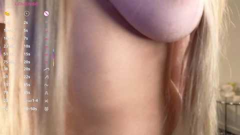 A close-up video of a fair-skinned woman's bare upper torso, focusing on her large, round breasts and erect nipples. Her long, blonde hair is visible in the background. The image includes a digital calendar with dates and tasks.