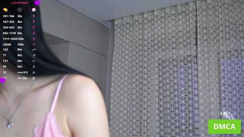 A video of a woman in a pink bra, facing away, with a detailed patterned curtain in the background. The image also features a live stream notification.