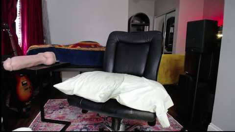 Media: Video of a dark-haired woman lying on a massage table, wearing a white towel, in a modern, dimly lit room with red curtains, black furniture, and a large speaker.
