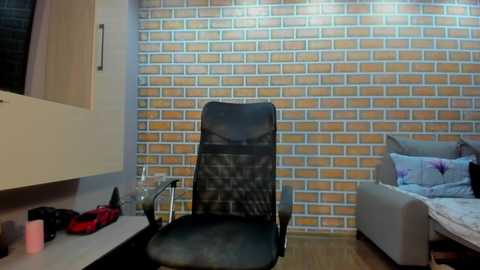 Video of a modern bedroom with a brick-patterned wallpaper, a black office chair, and a bed with floral pillows.