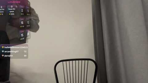 A video of a dimly lit room with a black metal chair facing a plain beige wall. A digital display on the wall shows user information and statistics in purple and white text.