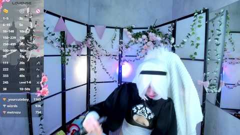 Video of a person dressed as a white bunny, wearing a black hoodie with a graphic, standing in a room adorned with pink floral decorations and a mirror.