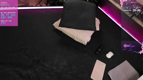 A video of a messy desk with scattered papers, a computer mouse, and a black pillow on a black mat. A video game controller and a pink cushion are also present.