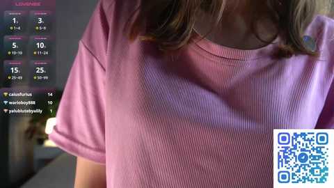 Media: A video of a woman's chest and shoulders in a light pink ribbed sweater, with a QR code in the bottom right corner.