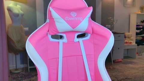Video of a pink and white gaming chair with a high backrest, featuring the \"dovetail\" logo, set in a modern, brightly lit room with shelves and a mannequin.