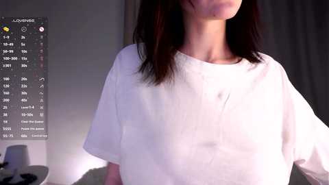 Video of a person with light skin and straight, shoulder-length dark brown hair, wearing a white, loose-fitting t-shirt, with a blurred background.