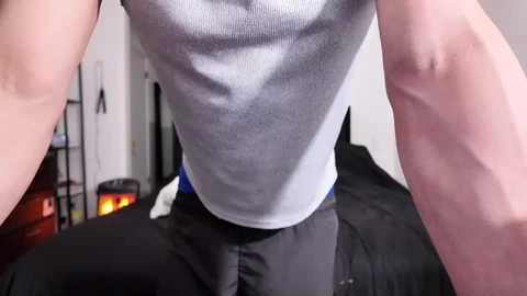 Video of a muscular, shirtless man with fair skin performing a push-up. He wears black athletic pants. Background features a blurred living room with a fireplace and shelves.