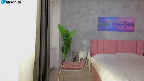 A modern, minimalist bedroom video featuring a light gray wall with a pink upholstered headboard, a green plant, and a colorful cityscape painting above a bed.