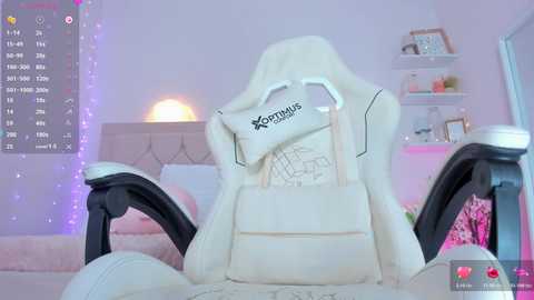 A video of a plush, white, ergonomic gaming chair with the \"Karmas\" logo, positioned in a pastel-colored, softly lit bedroom with pink accents, featuring a white bed and a shelf with decorative items.