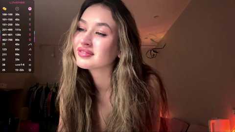 Media: Video of a light-skinned woman with long, wavy, blonde hair, wearing a low-cut top, puckering her lips. Background shows a dimly lit room with a closet and a red lamp.