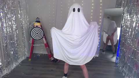 Media: A video shows a person in a white ghost costume, holding a red and yellow target, in a Halloween-themed room with silver streamers and string lights.