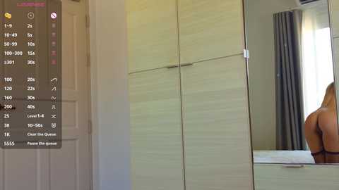 Video of a blonde woman's bare back in a modern bedroom with light wood wardrobe and gray curtains.