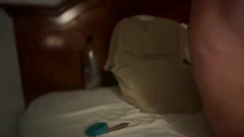 A dimly lit video shows a beige pillow on a bed with a wooden headboard. A blue pen lies on the pillow. The image appears to be taken in a bedroom setting, with muted colors and soft lighting.