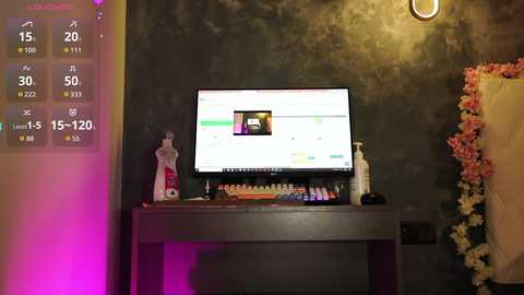 A video of a modern desk with a monitor displaying a video, a decorative flower arrangement, and a white vase with a red bow, set against a textured, dark wall.