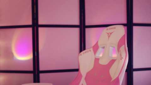 A video of a pink, plush chair with a cartoonish, smiling face in a room with large, pink-tinted window panels, creating a soft, dreamy ambiance.