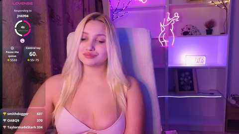 Video of a blonde woman in a white tank top, sitting on a chair, with purple neon lights and modern decor in the background.