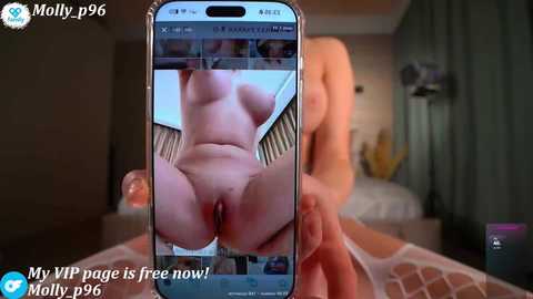 A video of a naked woman's bare buttocks and vulva, taken by a smartphone, with blurred background featuring a bed and a lamp.